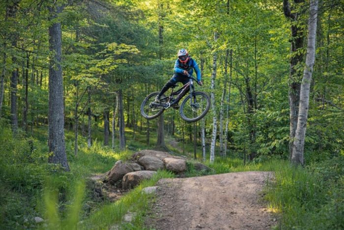 Ein Mountainbiker springt mit seinem Fully-Bike über eine Felsformation im Wald.